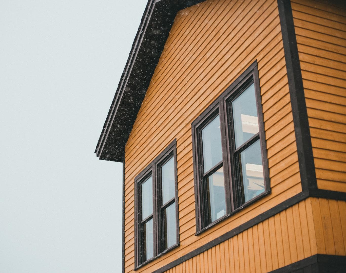 Lap siding, dark trim, and a roof eave on a home during falling snow