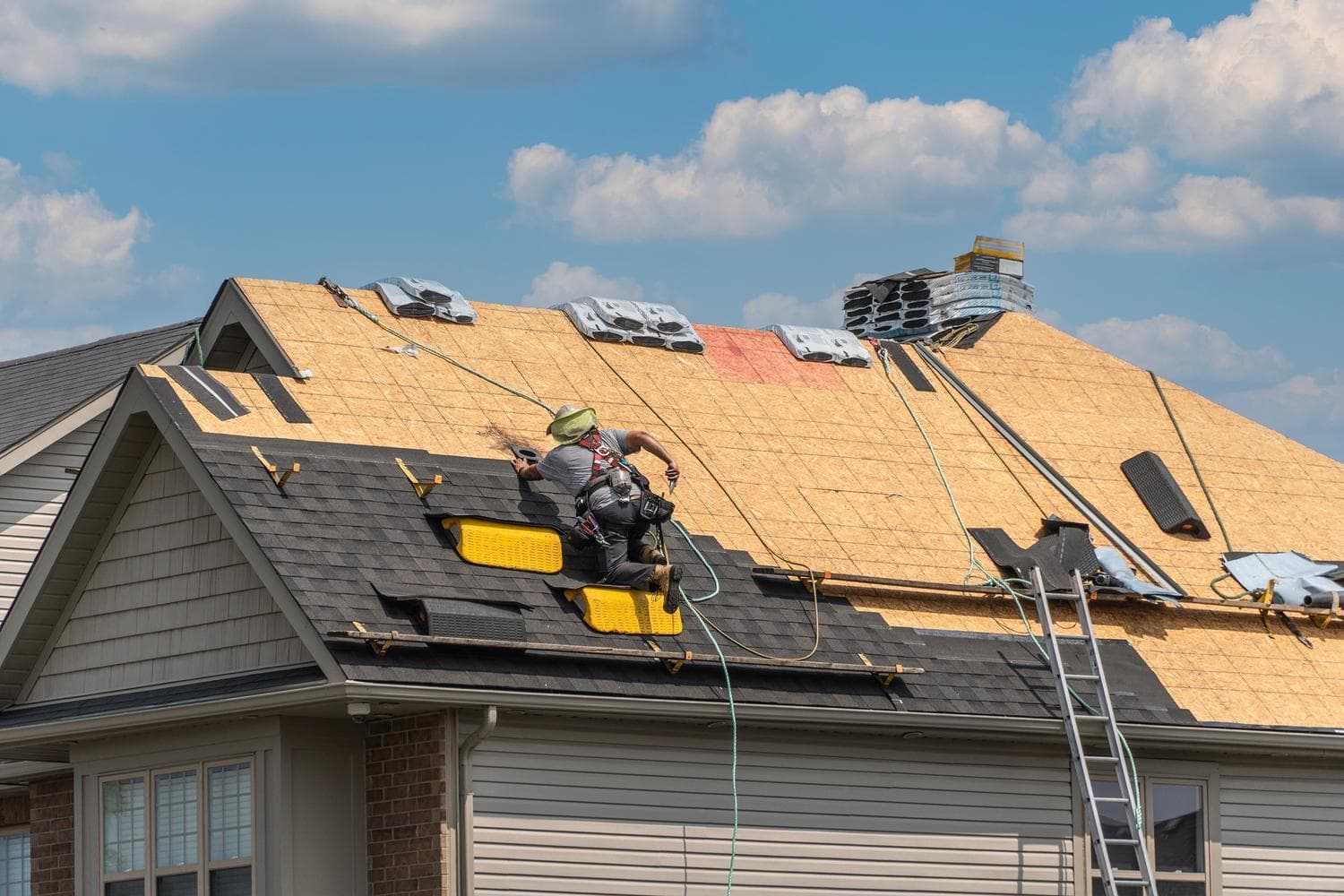 Roofer working on a tear-off with bare decking and roof jacks on a two-story home